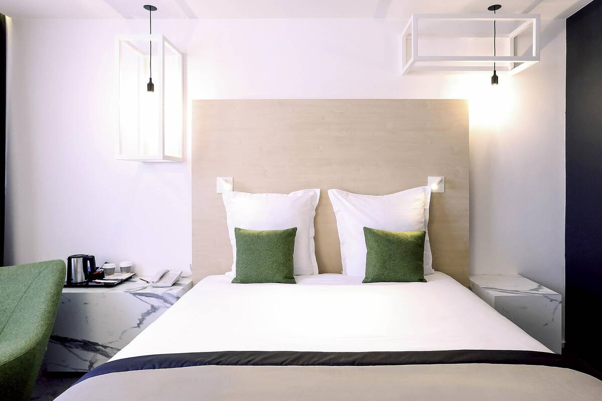 A hotel room with a bed, a green chair, a coffee maker, and a nightstand with a lamp.