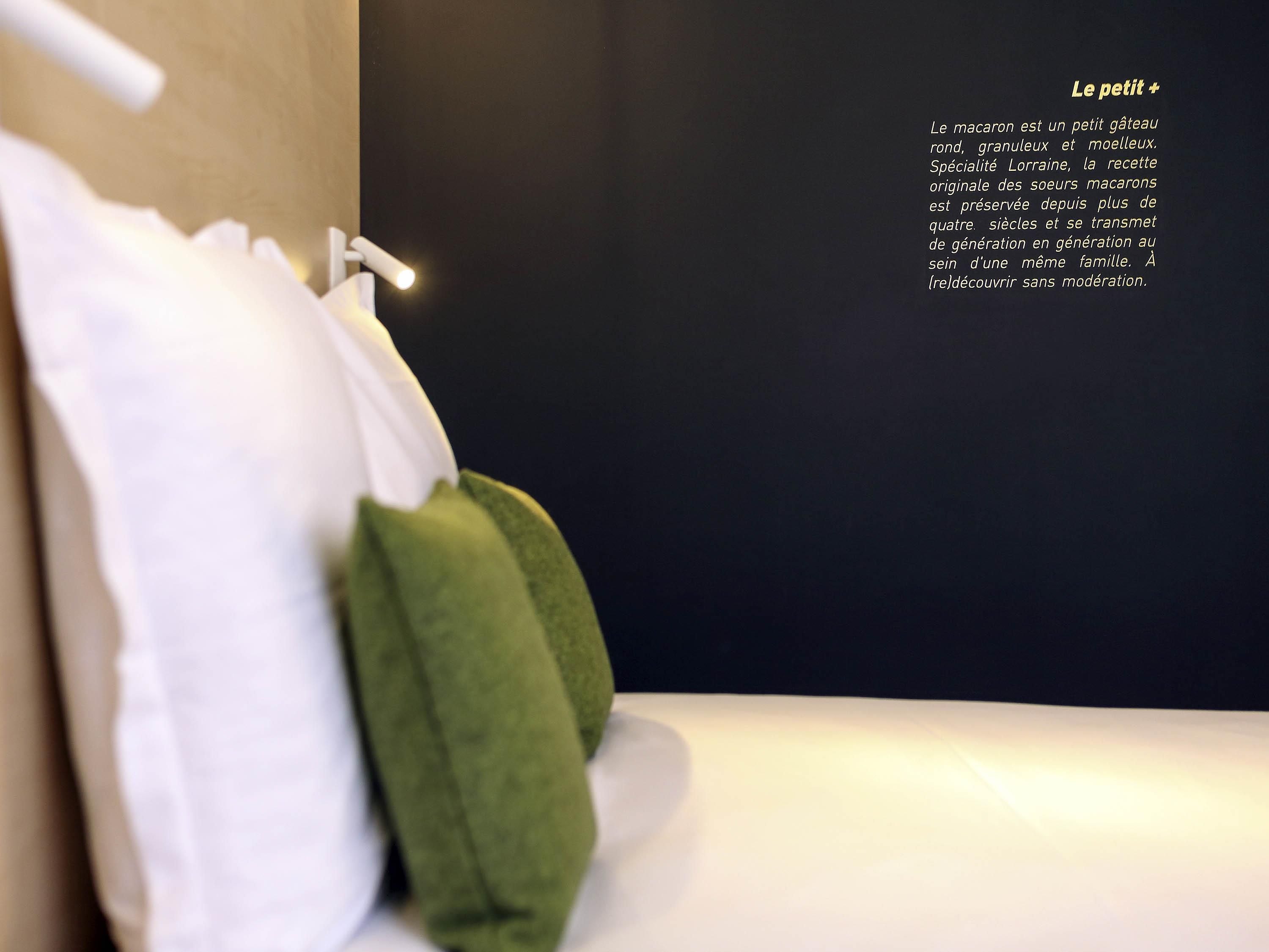 Una cama bien hecha con almohadas y una colcha blanca, una lámpara de pared y una descripción escrita en la pared.