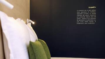 Una cama bien hecha con almohadas y una colcha blanca, una lámpara de pared y una descripción escrita en la pared.