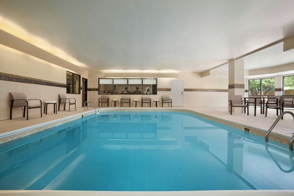 A swimming pool with chairs and tables around it, a door, and a window with a view of trees.