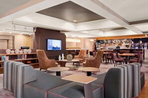 A modern lounge area with sofas, tables, a bar, and a television screen.
