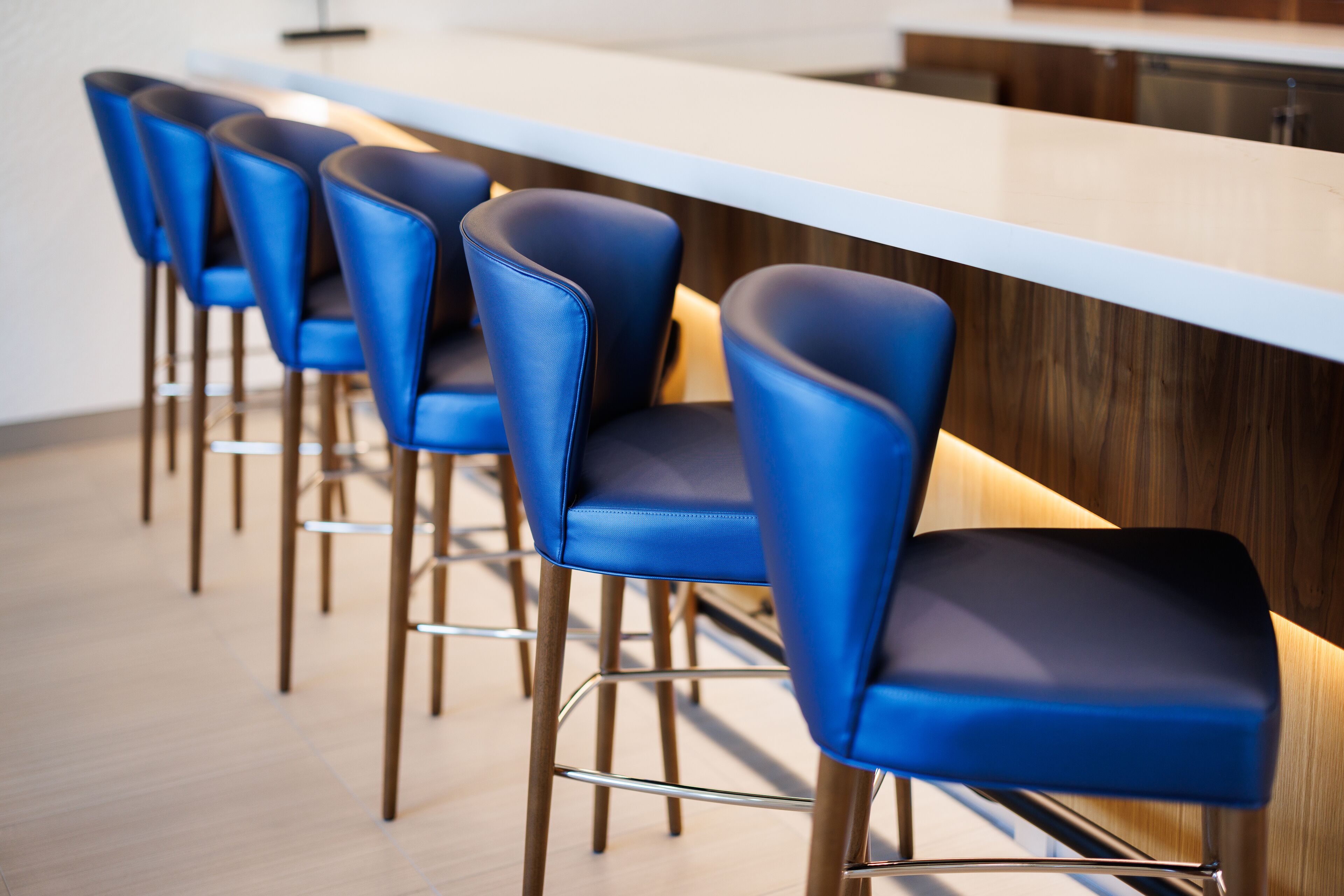 A row of blue bar stools with metal legs and a wooden bar in a modern interior.