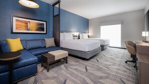 A hotel room with a blue wall, a large bed, a sofa, a desk, and a chair.