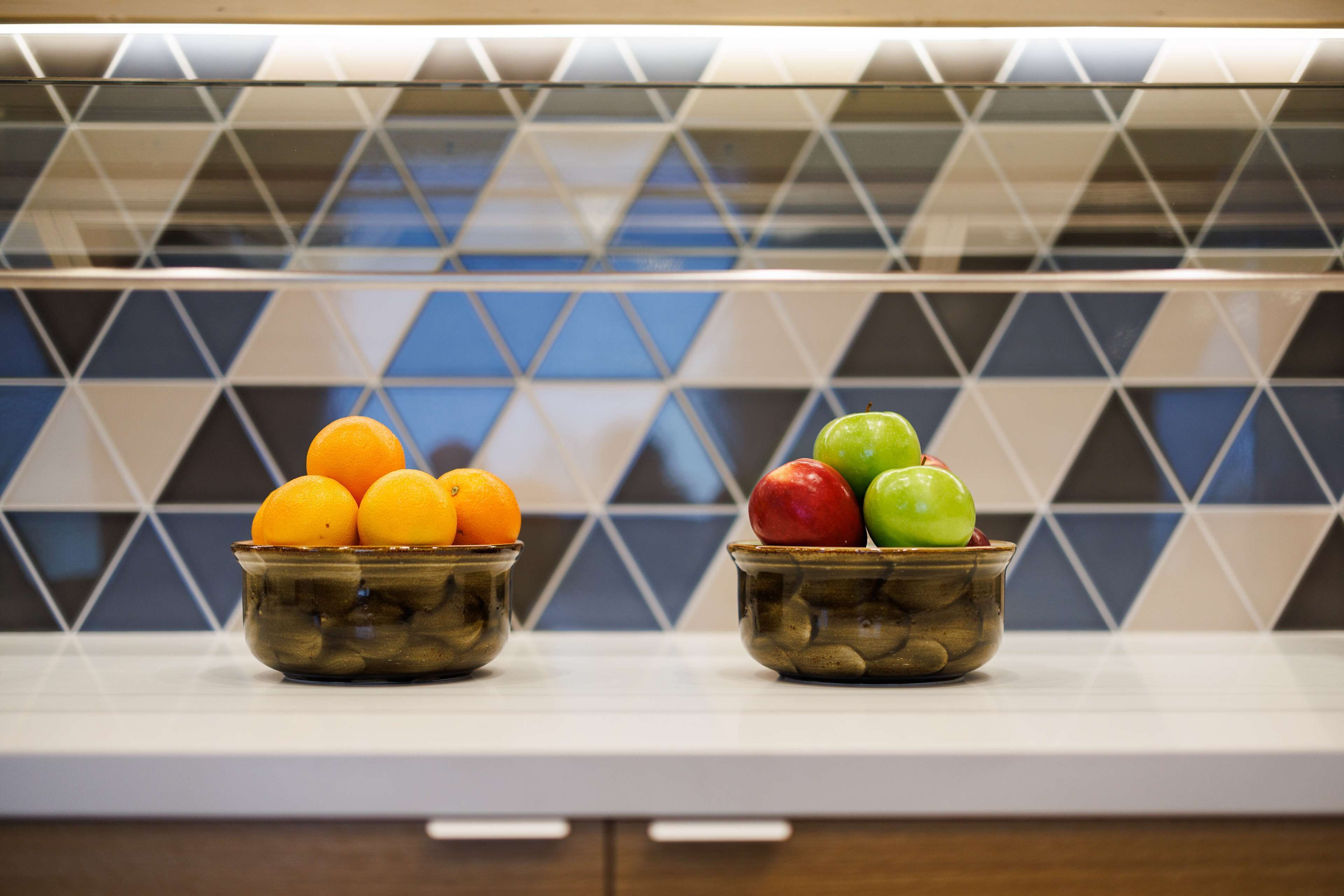 Duas tigelas de fruta em uma bancada de cozinha com um painel de azulejos geométricos.