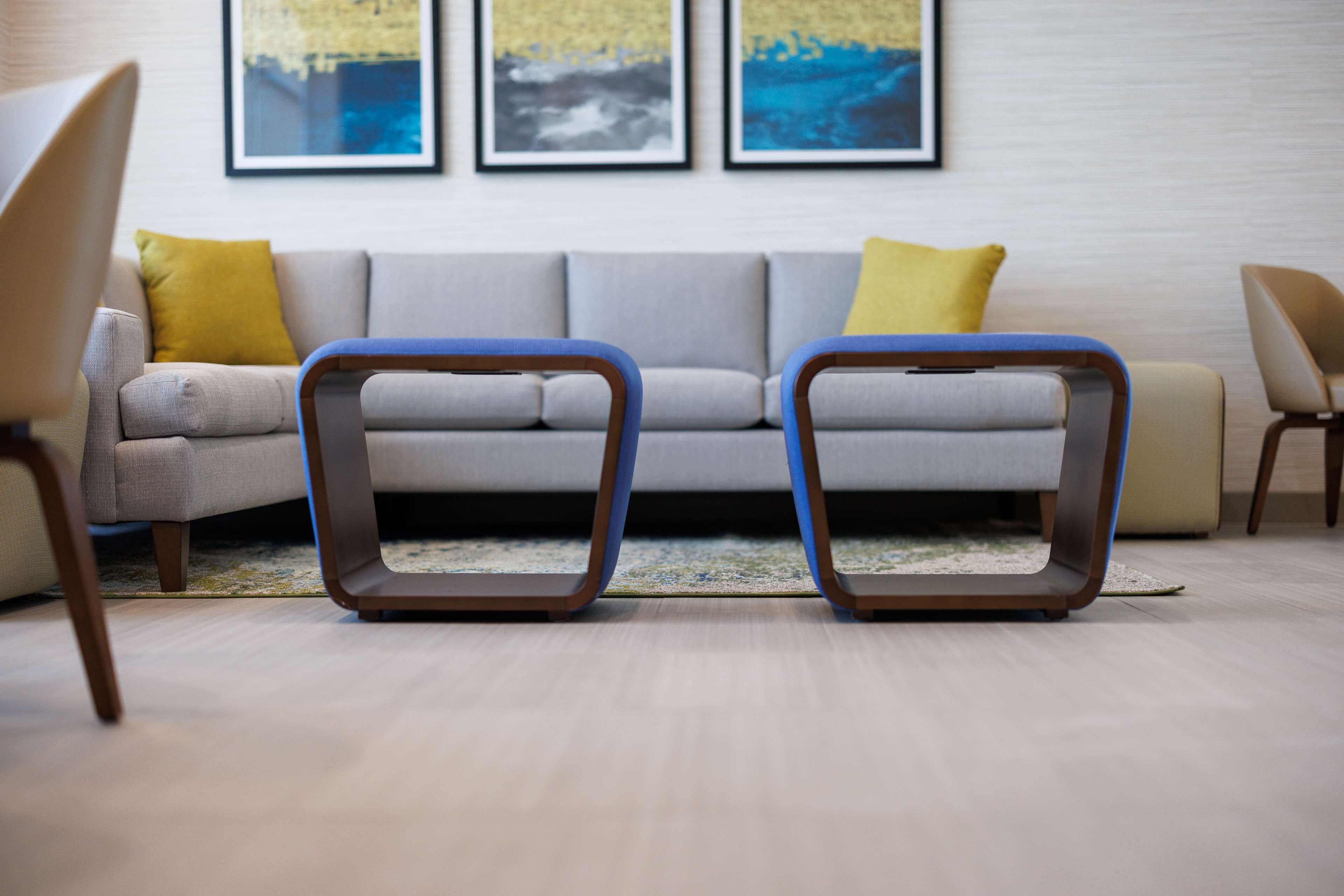 A modern living room with a grey sofa, two blue and brown chairs, and yellow cushions.