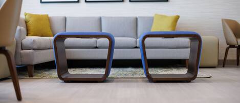 A modern living room with a grey sofa, two blue and brown chairs, and yellow cushions.