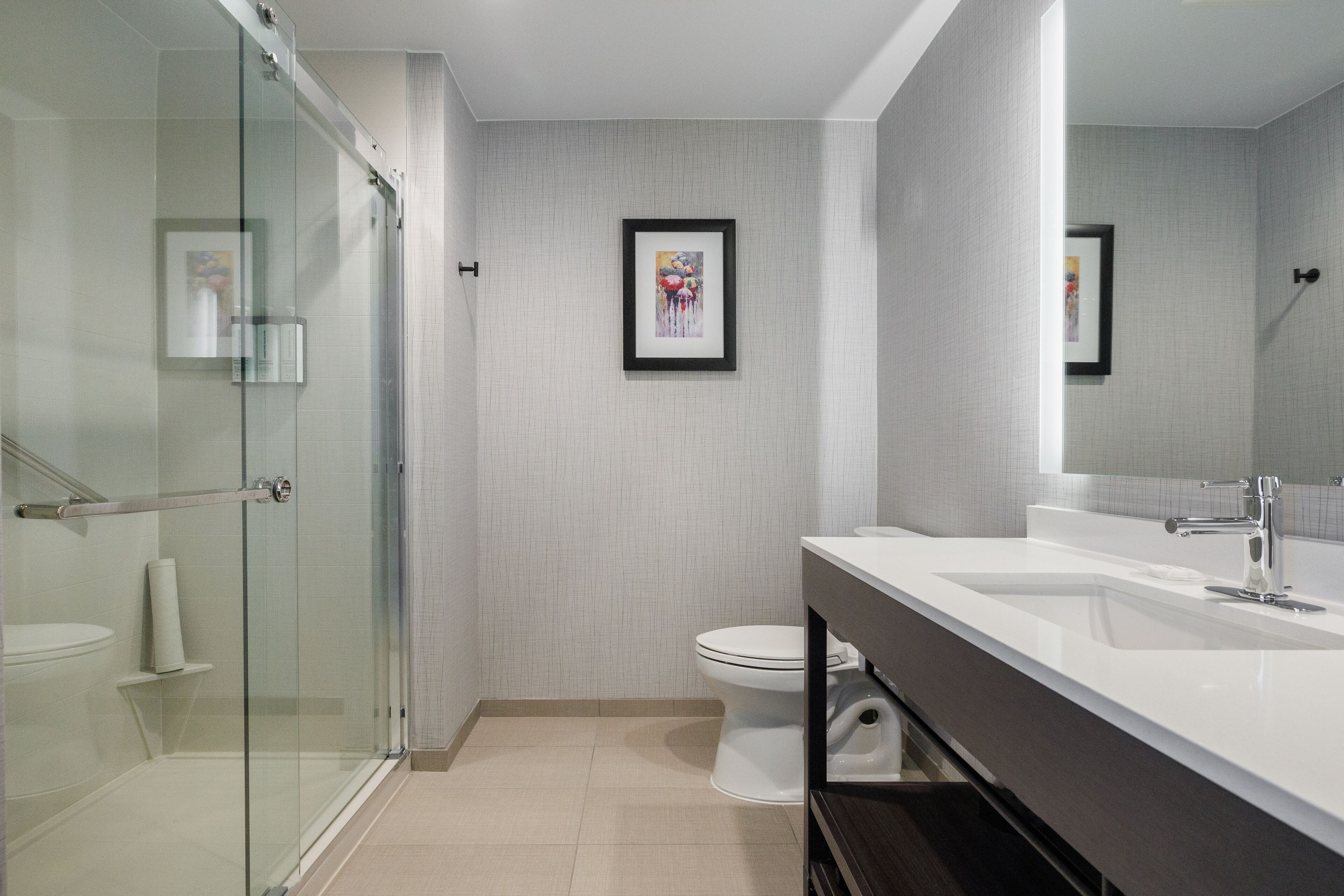 A modern bathroom with a glass shower enclosure, a white toilet, and a large mirror above the sink.