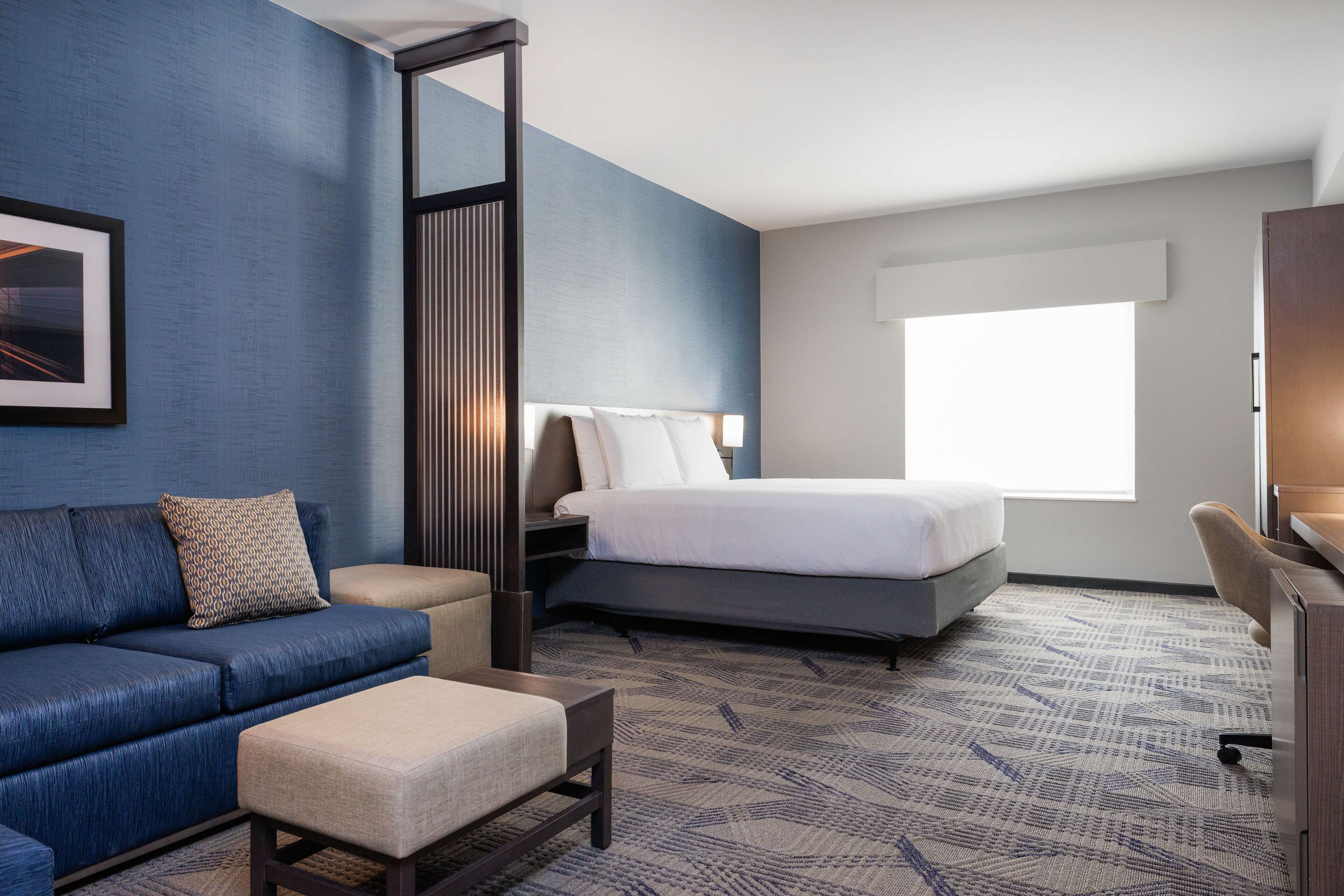 A hotel room with a bed, a sofa, a desk, and a large window.