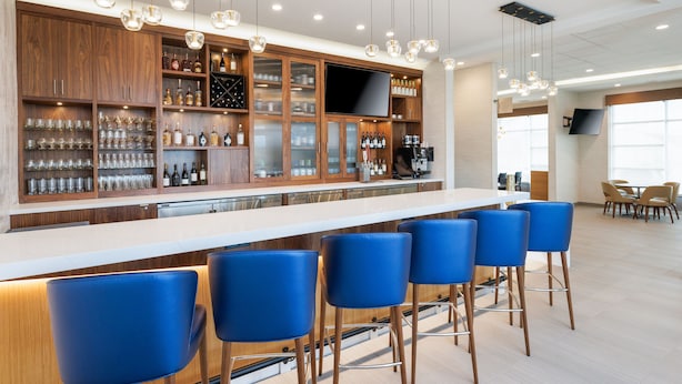 A modern bar area with wooden cabinets, a flat-screen TV, and blue bar stools.