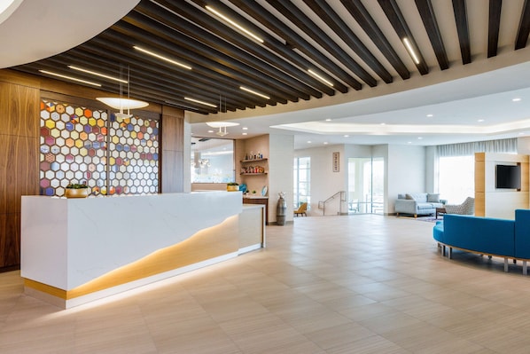 A modern reception area with a white reception desk, wooden paneling, and a colorful hexagonal wall design. - Hyatt Place San Carlos (San Carlos)