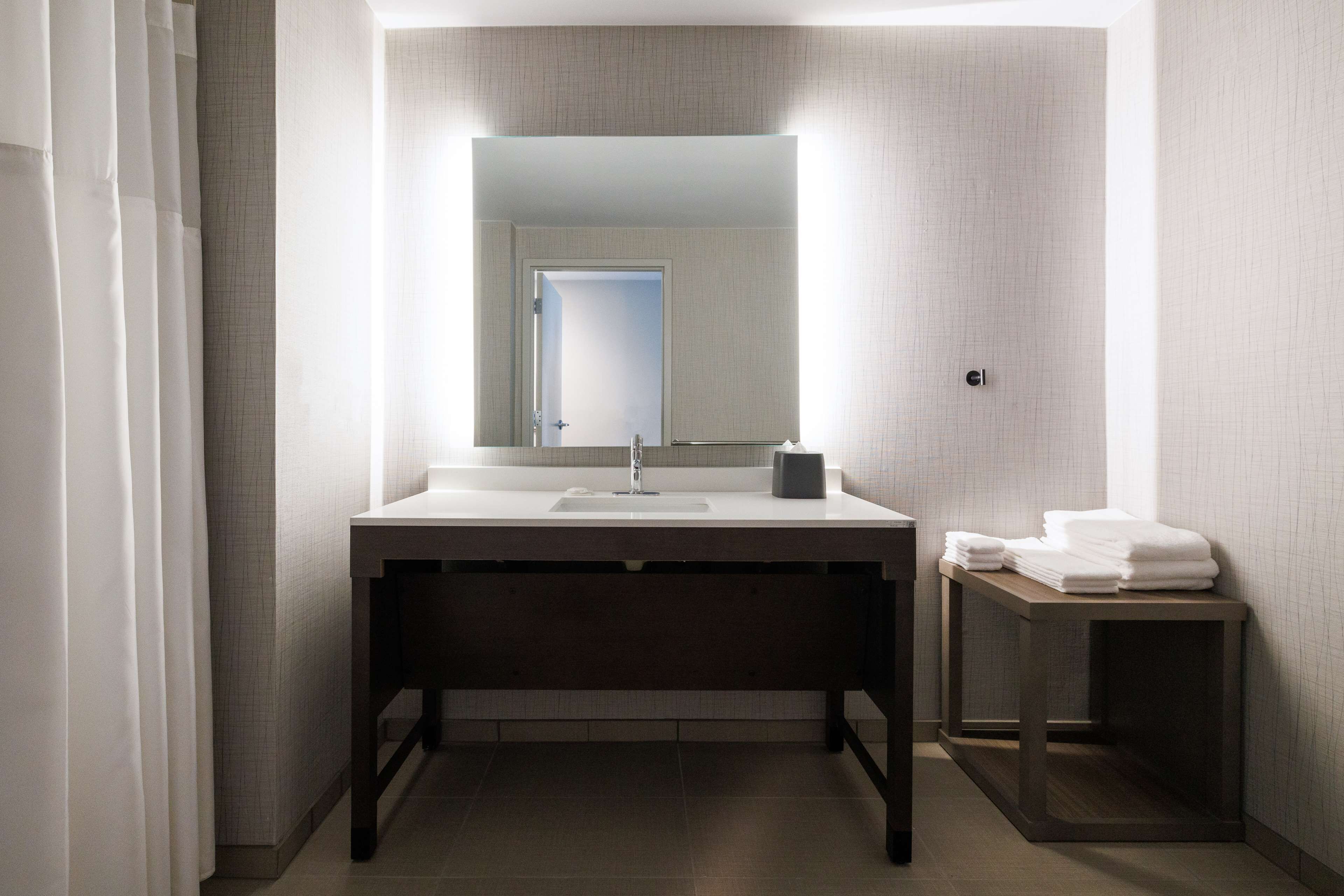 A modern bathroom with a large mirror, a sink, and a small table with towels.