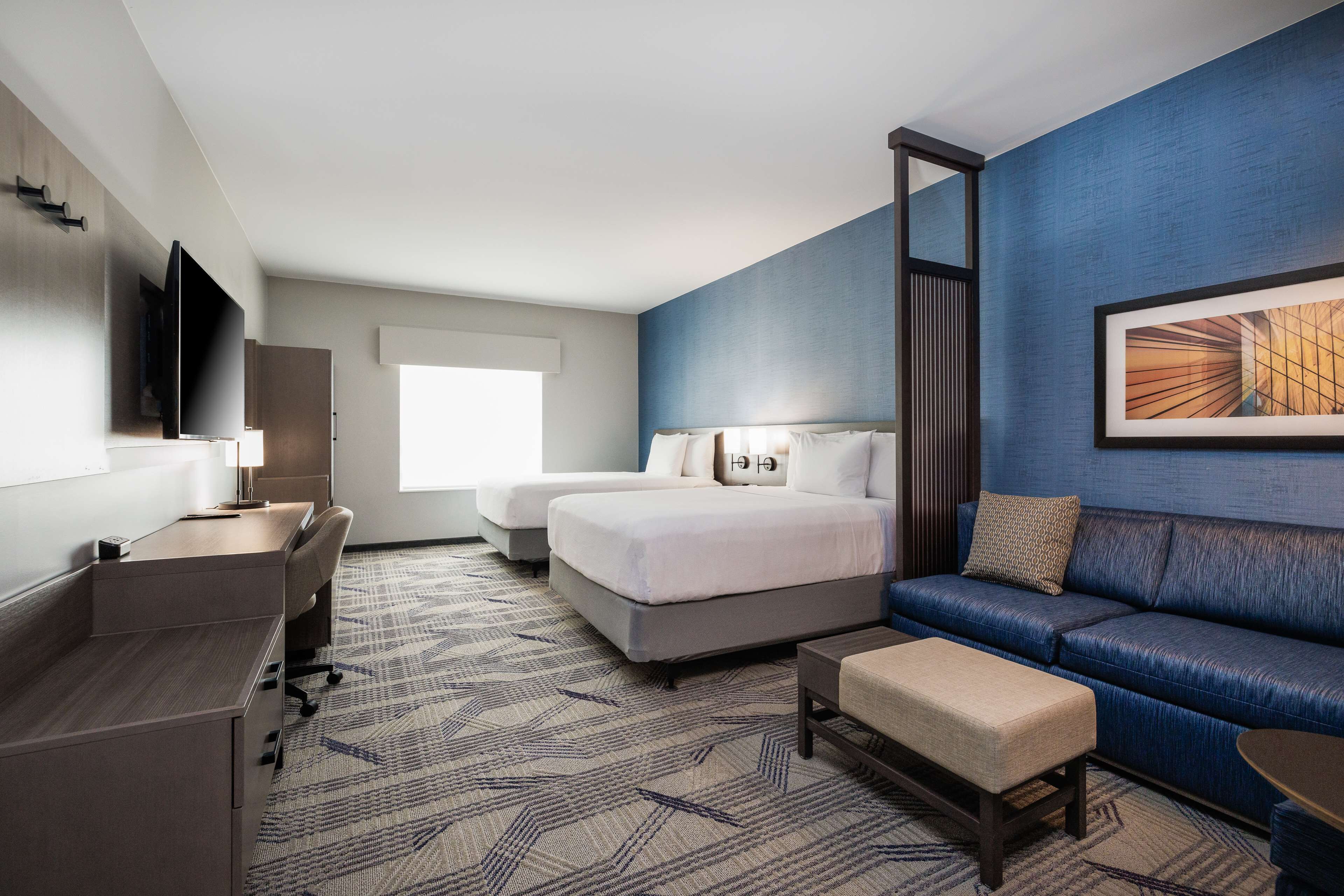 A hotel room with a bed, a sofa, a desk, and a TV.