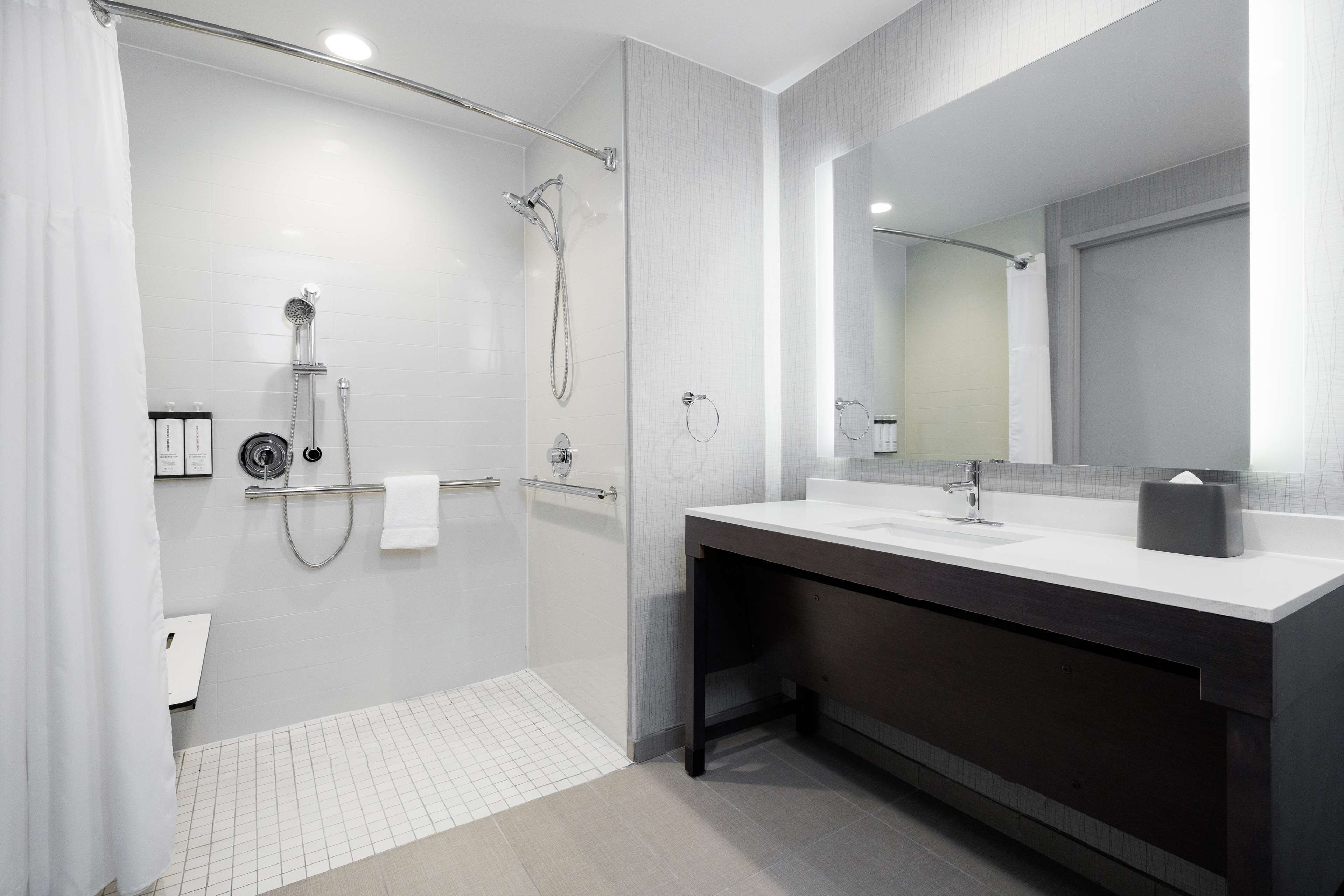 A modern bathroom with a glass-enclosed shower, a dark vanity with a white sink, and a large mirror.