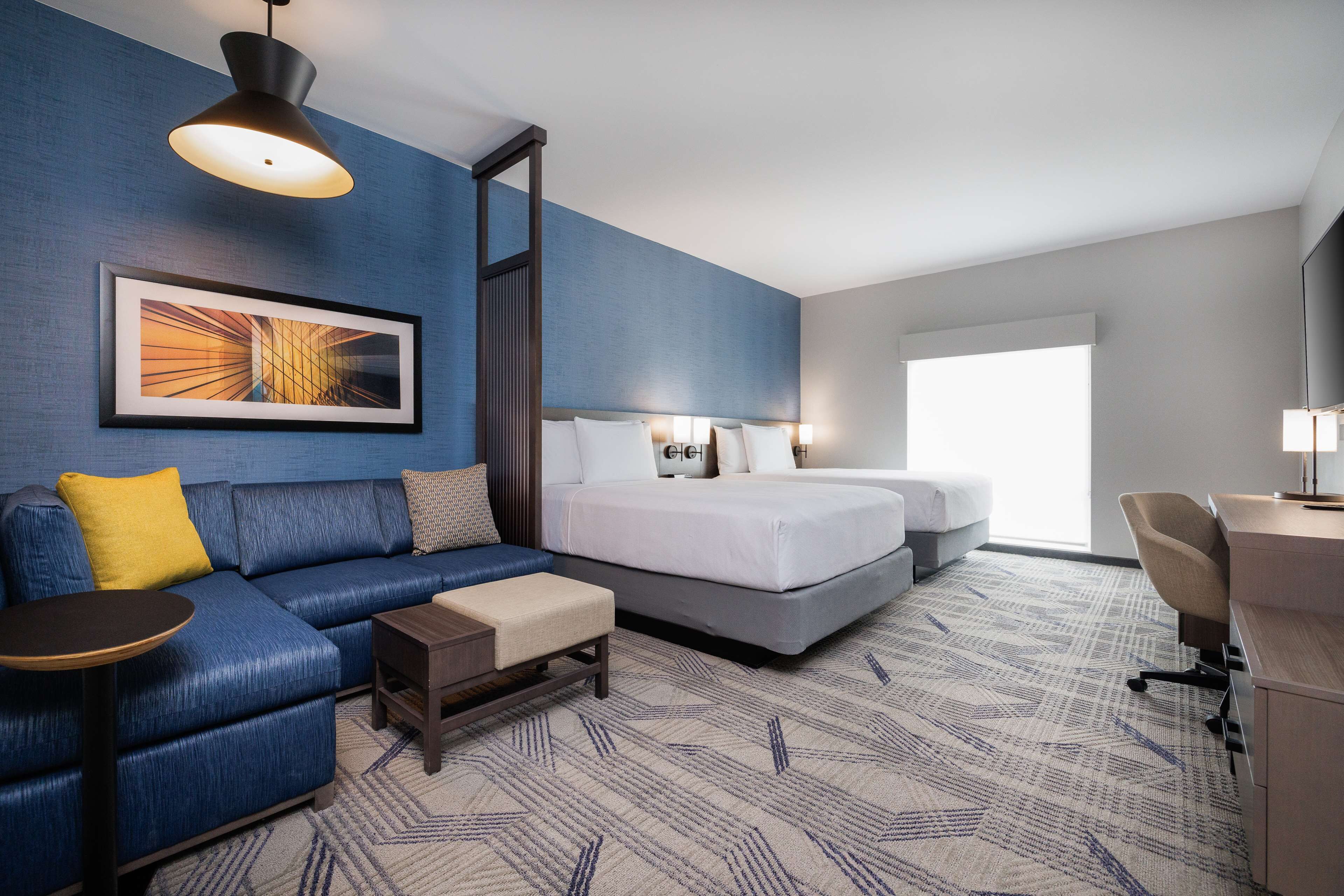 A hotel room with a blue sofa, a bed, a desk, and a large window.