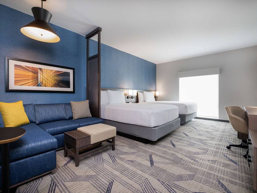 A hotel room with a blue sofa, a bed, a desk, and a large window.