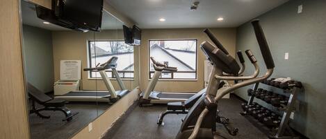 Une salle de sport équipée de matériel d’exercice, d’un tapis de course et d’un miroir.