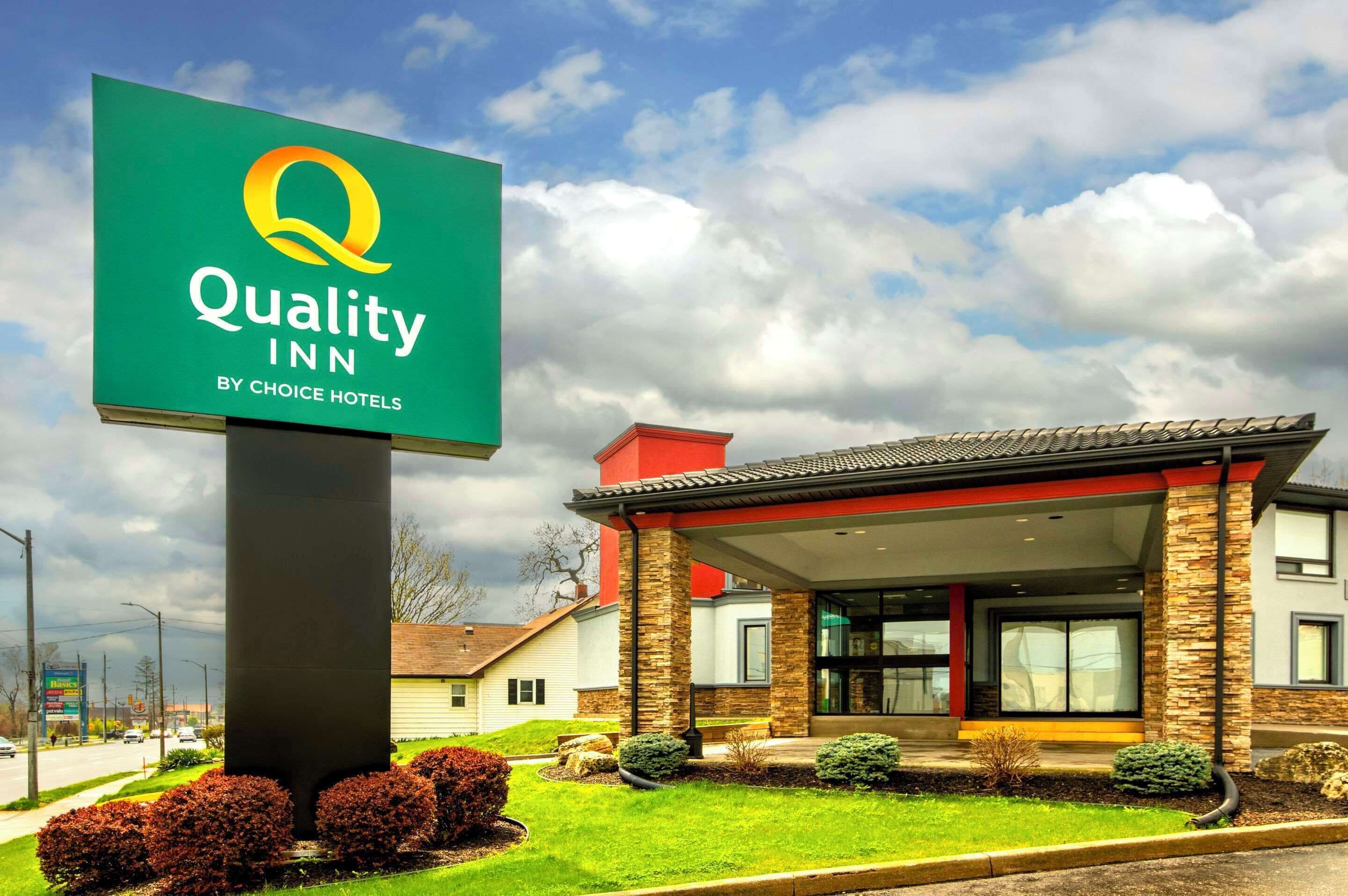 A hotel sign with a logo and name, a building with a modern design, and a well-maintained lawn.