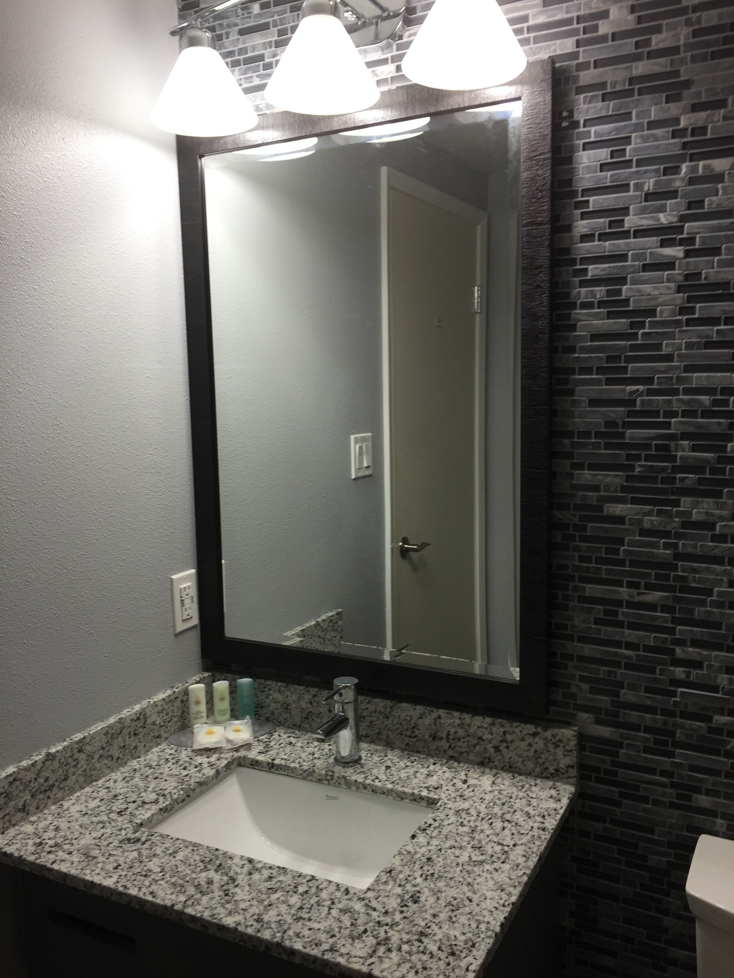 A bathroom with a granite countertop, a sink, a mirror, and a door.