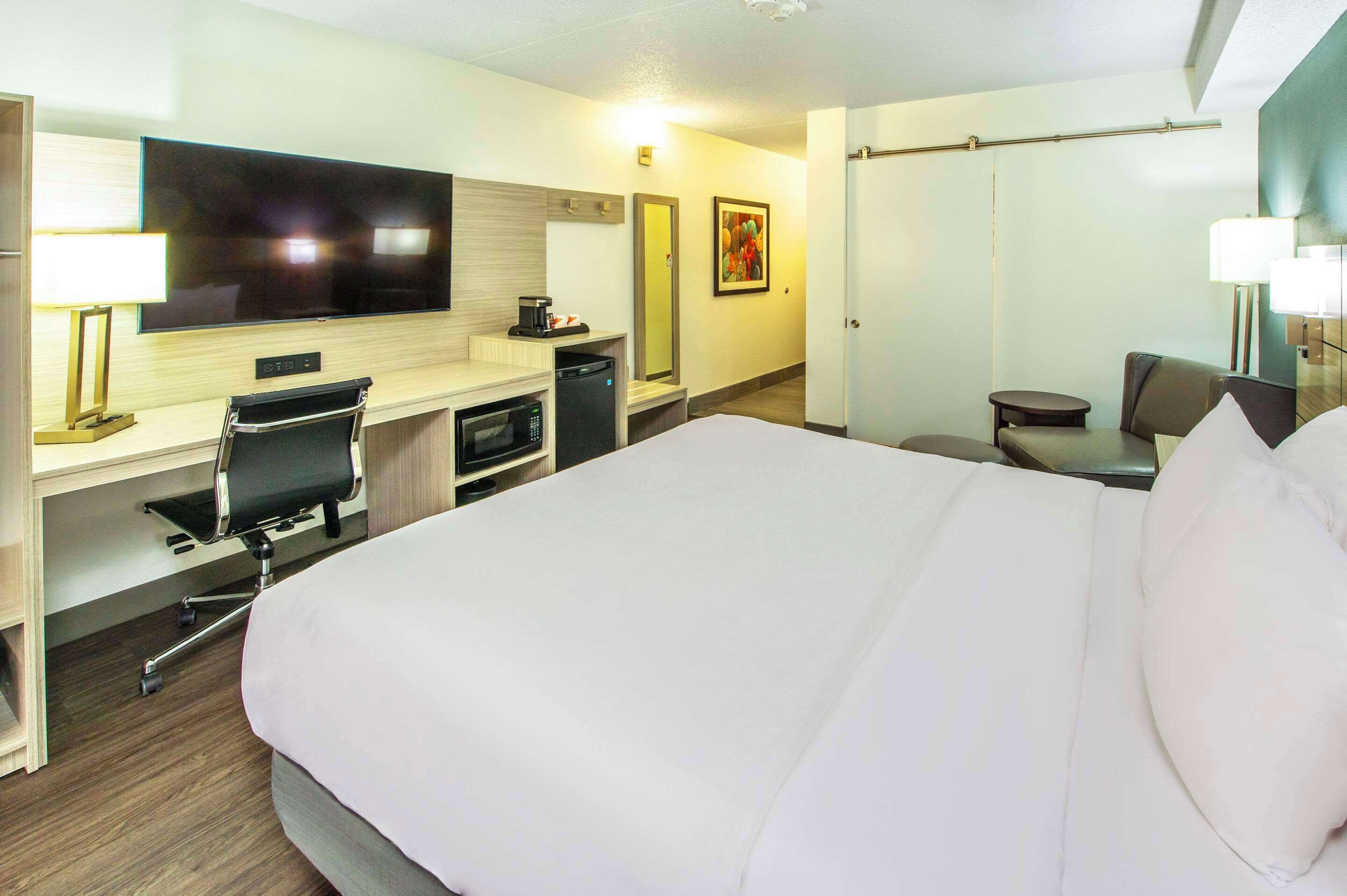 A hotel room with a large bed, a desk with a chair, a television, a coffee machine, and a small table with a chair.