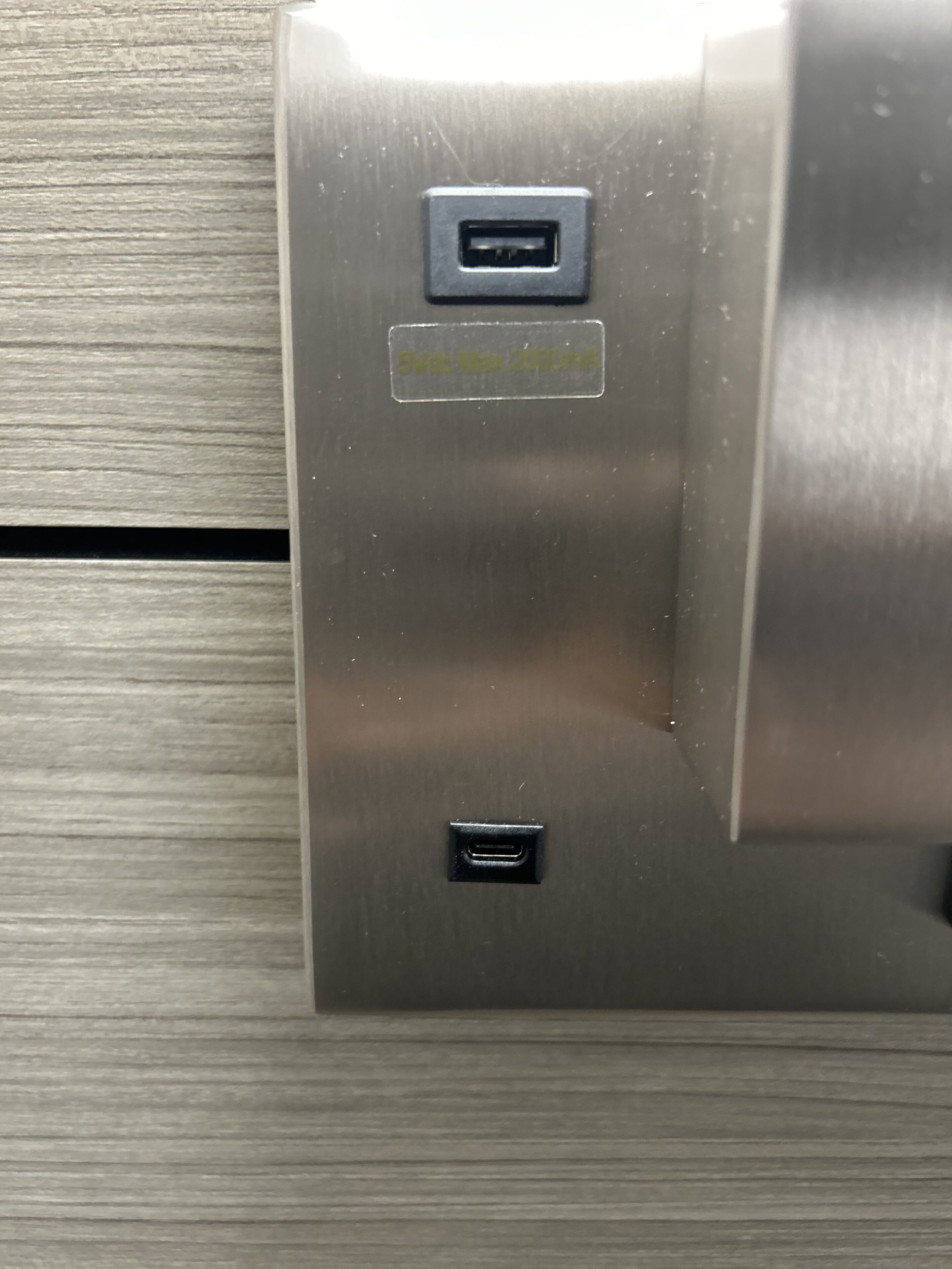 Superficie metálica con dos puertos USB y una etiqueta que dice "5V 2.1A".