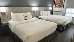 A hotel room with two beds, a dark wood floor, a grey accent wall, and a framed picture on the wall.