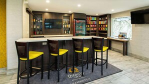 A bar area with a counter, bar stools, a refrigerator stocked with beverages, and shelves with snacks.