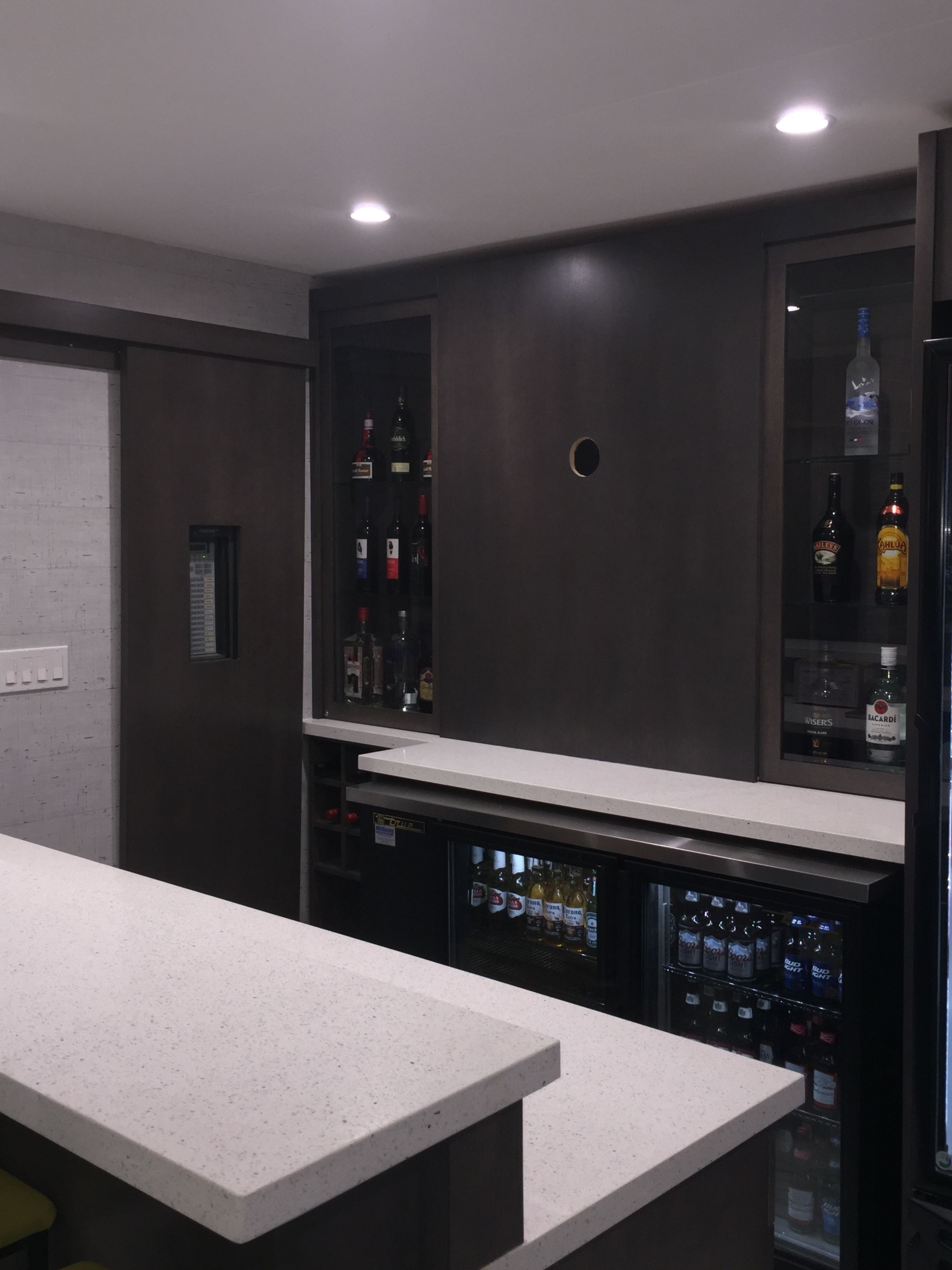 A modern bar area with a white countertop and shelves stocked with liquor bottles.