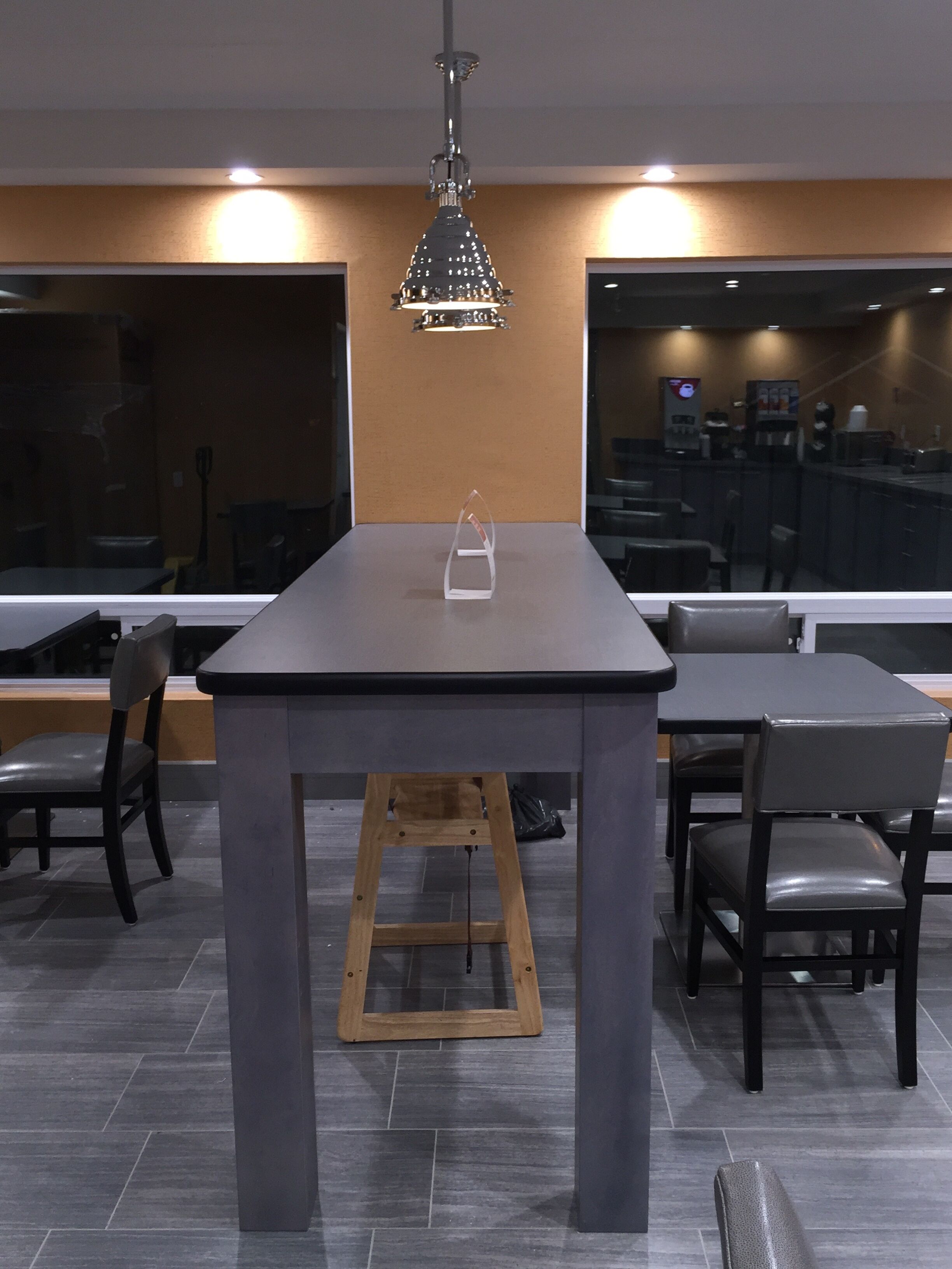 A modern dining area with a rectangular table, two chairs, a wooden stool, and a hanging pendant light.