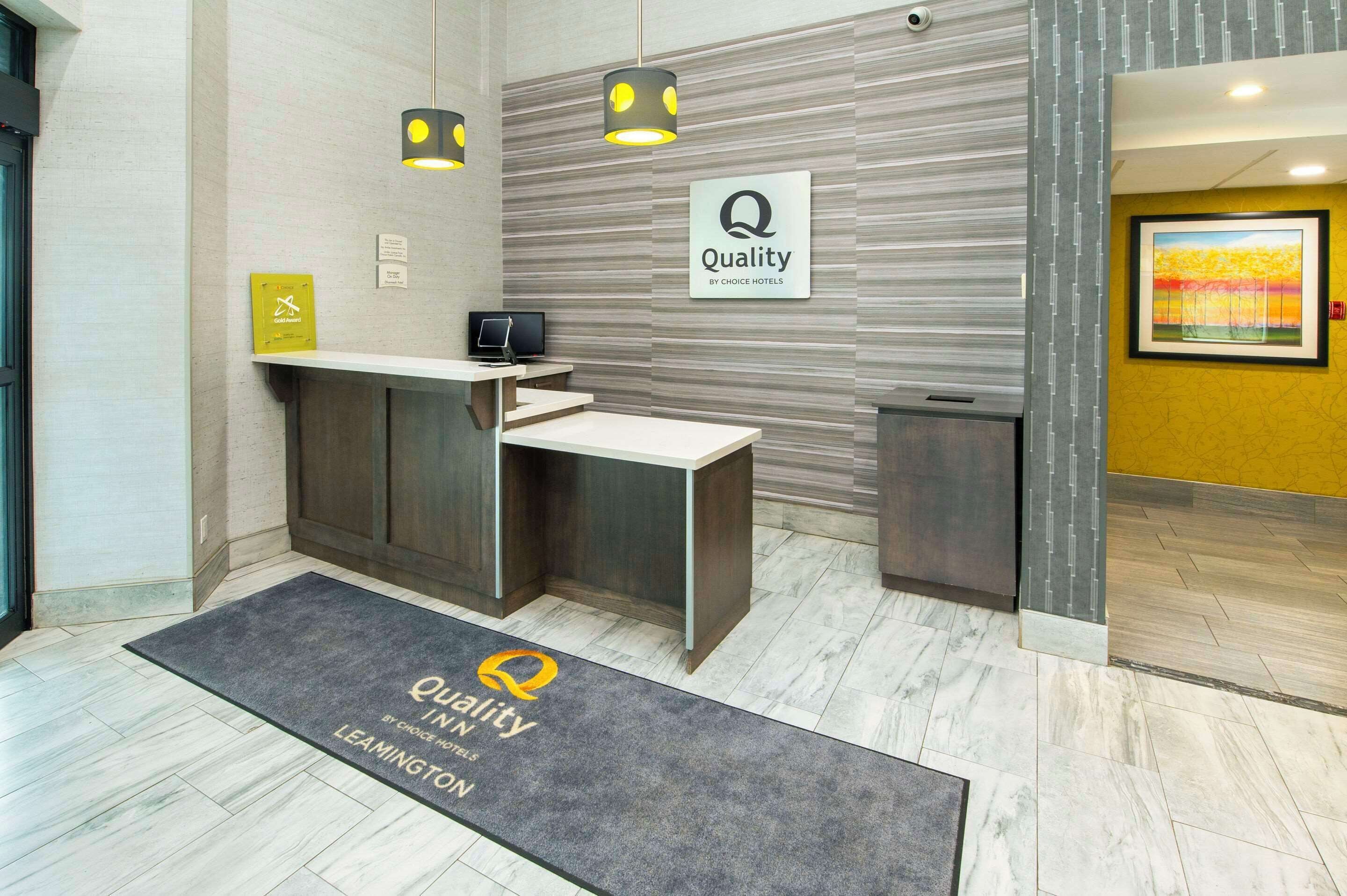 A hotel reception area with a reception desk, a digital screen, and a sign indicating 'Quality by Choice Hotels'.