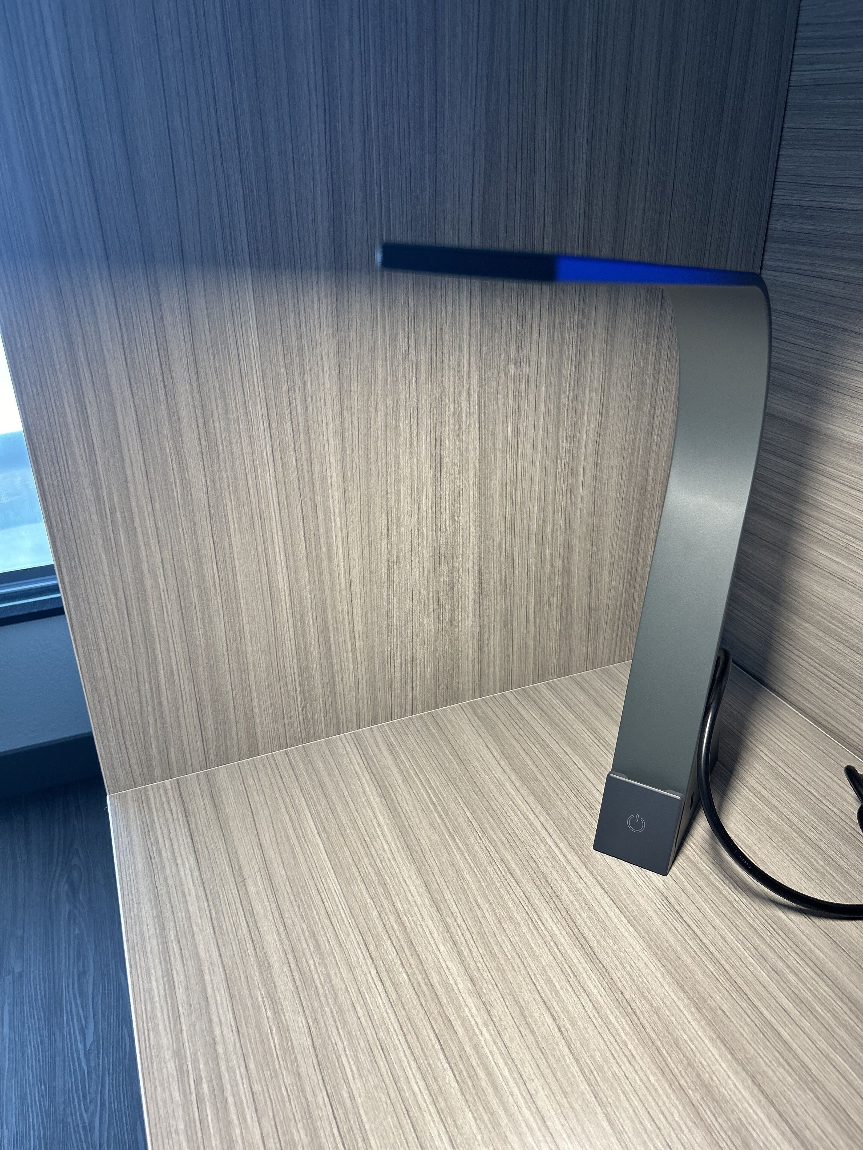 Una habitación moderna y minimalista con suelo de madera y un objeto metálico elegante, posiblemente un altavoz o estación de carga, sobre una estantería de madera.