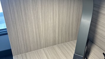 Una habitación moderna y minimalista con suelo de madera y un objeto metálico elegante, posiblemente un altavoz o estación de carga, sobre una estantería de madera.