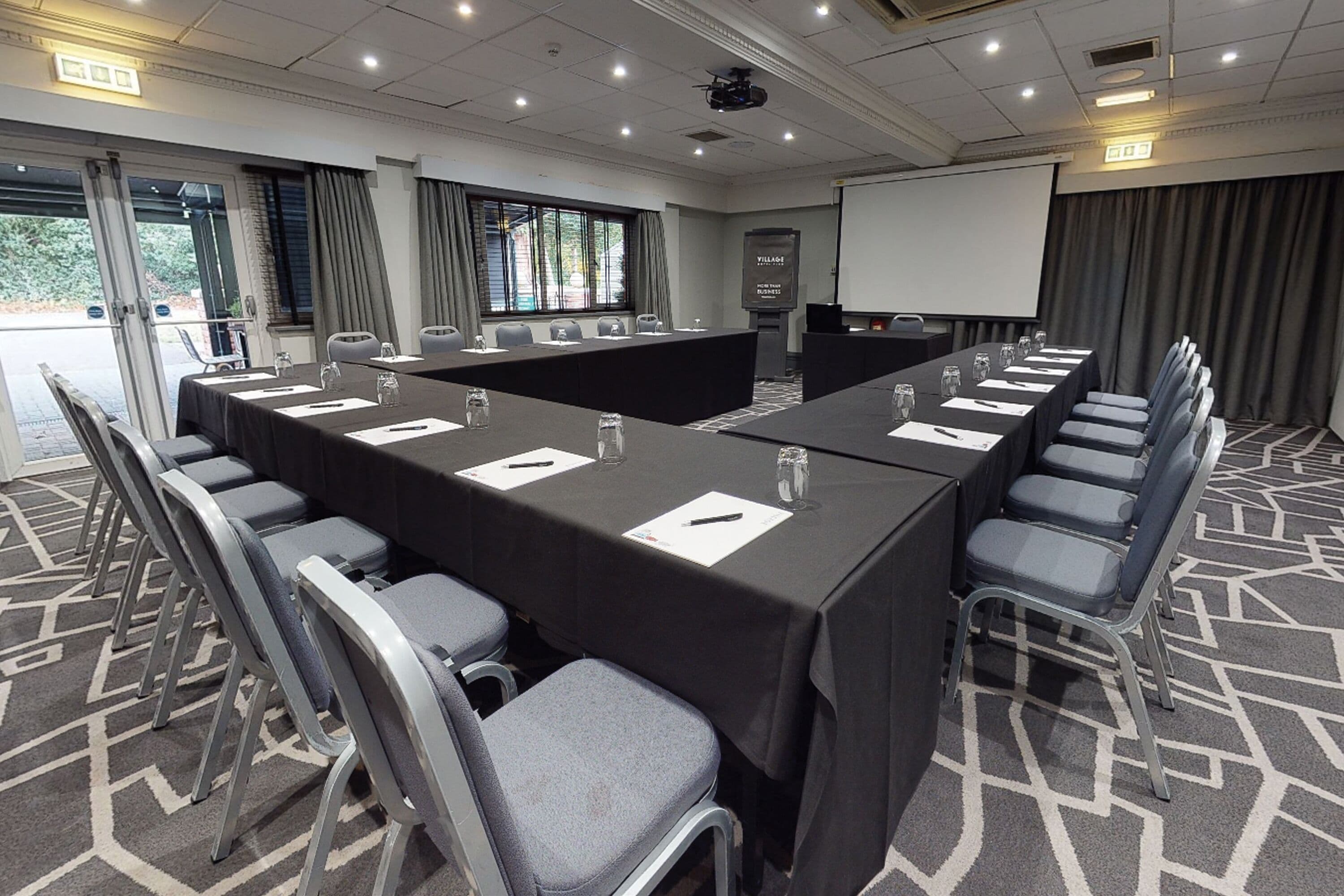 A conference room with a long table, multiple chairs, a projector screen, and a presentation screen.