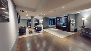 A modern lobby with a wooden floor, a seating area with sofas, a cash machine, and a visible entrance to the meeting rooms. - Village Hotel Manchester Cheadle (Cheadle)
