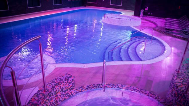 A swimming pool with a circular hot tub, surrounded by patterned steps and a tiled deck. - Village Hotel Manchester Cheadle (Cheadle)