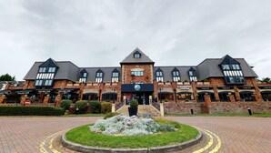 A large brick building with multiple storefronts, including a Village Pub and Starbucks Coffee. - Village Hotel Manchester Cheadle (Cheadle)
