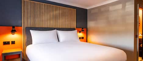 A hotel room with a large bed, bedside lamps, a small table, and a wooden headboard.
