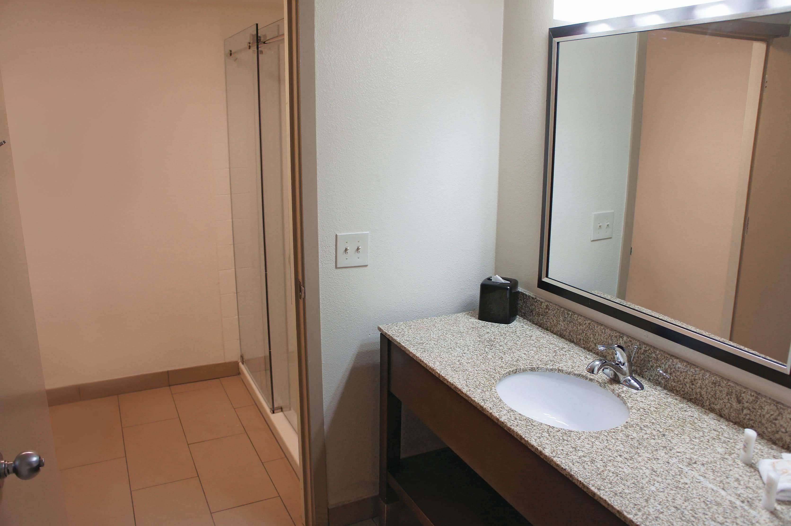 A bathroom with a glass shower door, a sink with a mirror, and a towel dispenser.