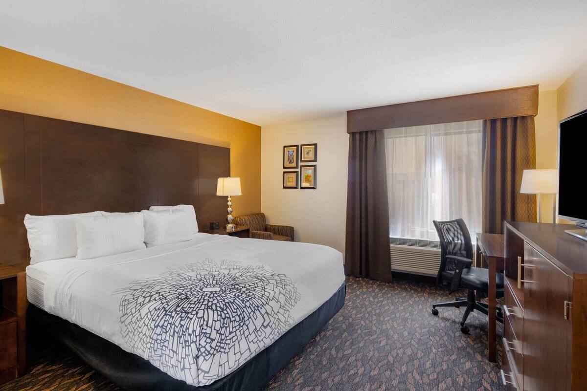 Een hotelkamer met een groot bed, een bureau, een stoel, een televisie en een raam met gordijnen.