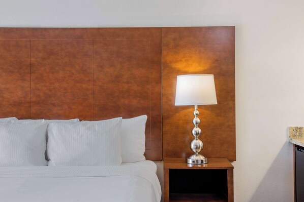 A neatly made bed with white linens and pillows, a wooden headboard, and a bedside table with a lamp.