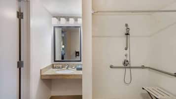 Une salle de bain équipée d’un lavabo, d’un miroir et d’une douche à l’italienne avec des barres d’appui.