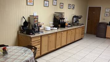 A clean, well-lit room with a long counter, a coffee machine, and a waffle maker. There are framed pictures on the wall and a door in the background.