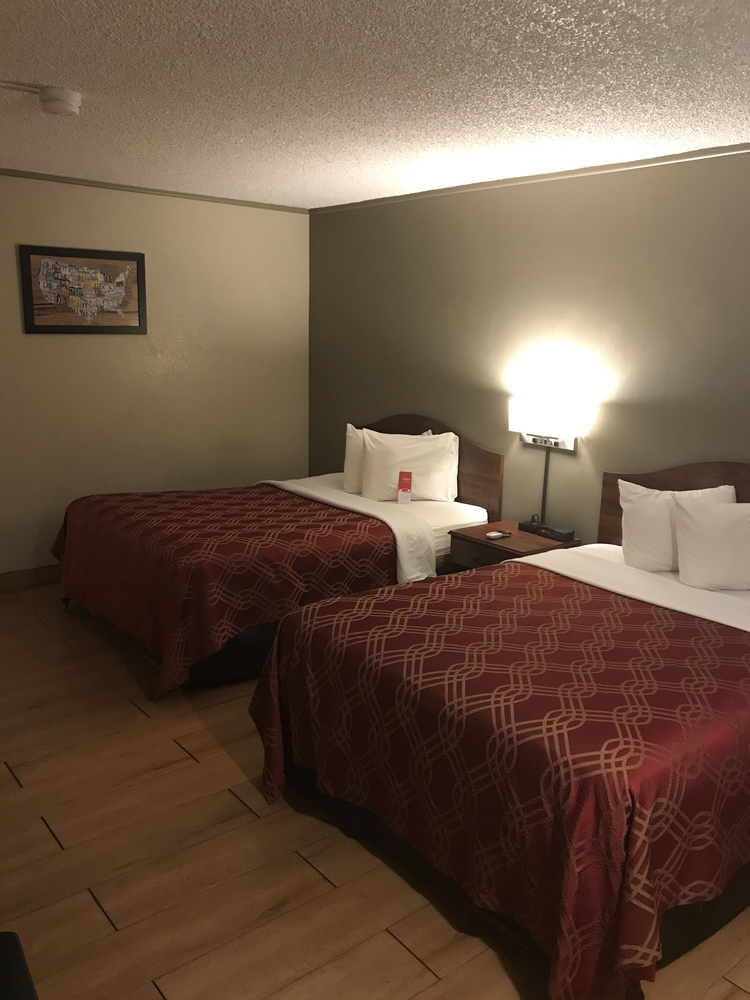 Habitación de hotel con dos camas, cada una con una colcha de rayas rojas, una mesita de noche, una lámpara y una luz empotrada en la pared.