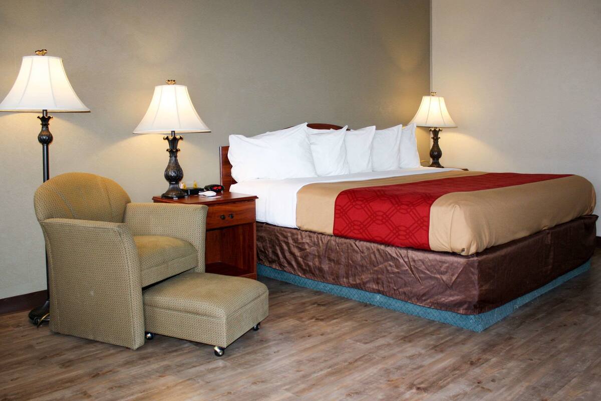 Una habitación de hotel con una cama, dos lámparas, una silla y una mesita de noche.