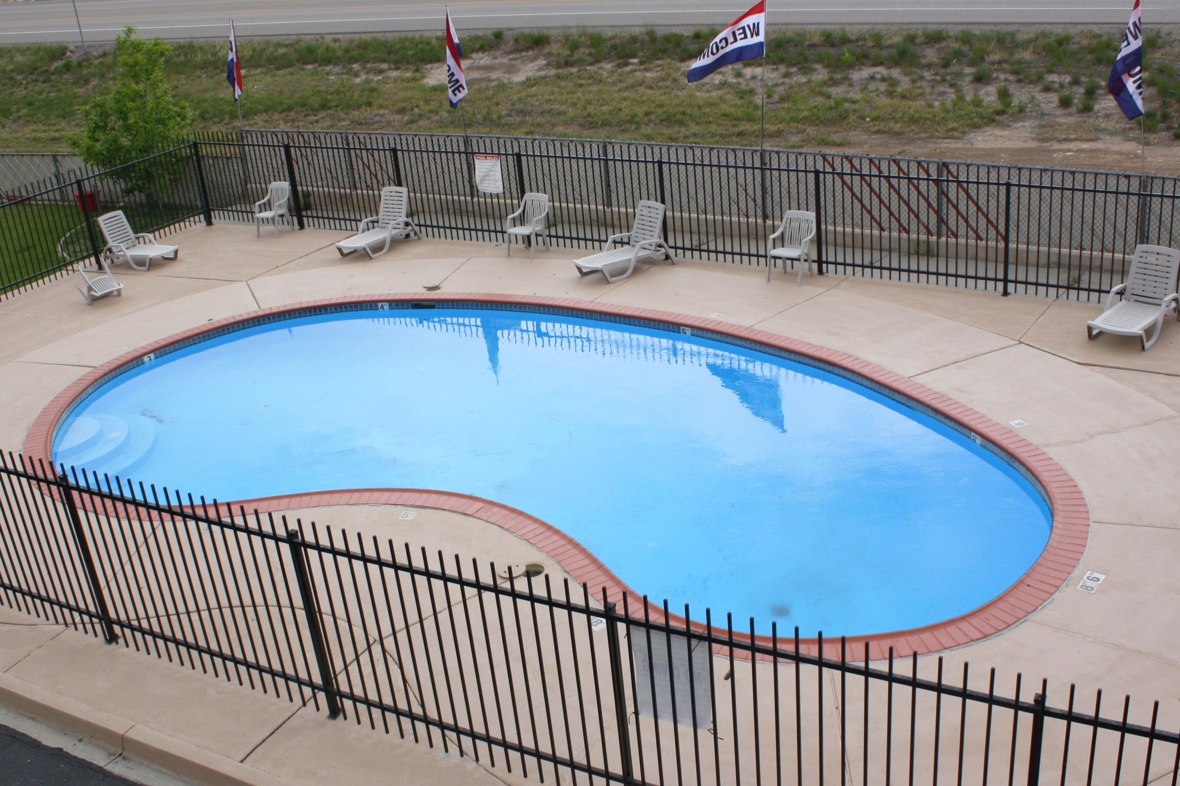 A swimming pool with a black metal fence, surrounded by lounge chairs and flags.