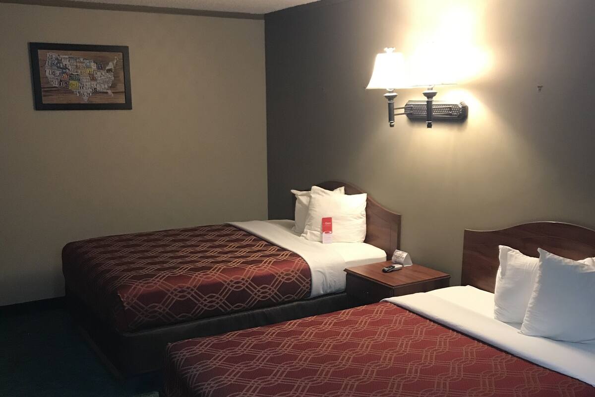 Habitación de hotel con dos camas, una mesita de noche, una lámpara y un aplique de pared.