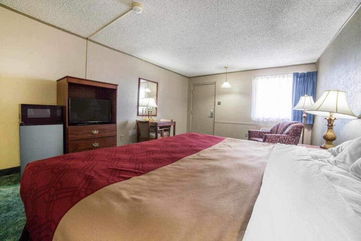 Habitación de hotel con cama, televisor, escritorio, silla y ventana con cortinas.