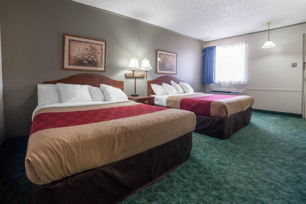 Habitación de hotel con dos camas, una ventana con cortinas, una lámpara y un cuadro colgado en la pared.