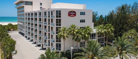 Un hotel de varios pisos con el logotipo de Marriott, rodeado de palmeras y una vista despejada de la playa.