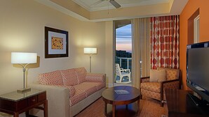 Een hotelkamer met een bank, fauteuil, televisie en een balkon met gordijnen.