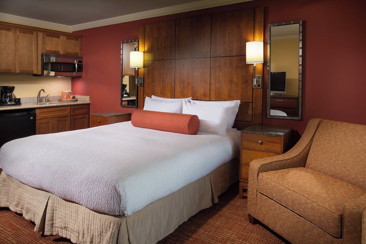 Ein Hotelzimmer mit Bett, Sessel, Schreibtisch mit Lampe, Mikrowelle und Kaffeemaschine.